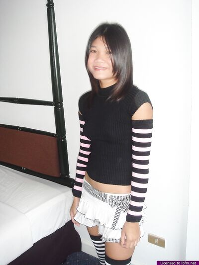 Νεαρή Ασιάτισσα πίνει μπύρα ενώ βγάζει τα ρούχα της για να φορέσει τις κάλτσες και τις κάλτσες της μέχρι τους μηρούς